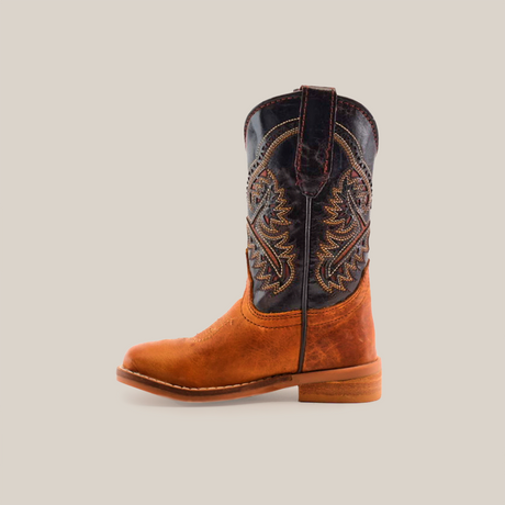 The Cater Honey Square Toe cowboy boot, crafted from cowhide leather, features a brown lower half and a dark upper shaft with intricate stitching. Its handcrafted design with a flat sole and almond-shaped toe exudes rustic elegance against a plain white background.