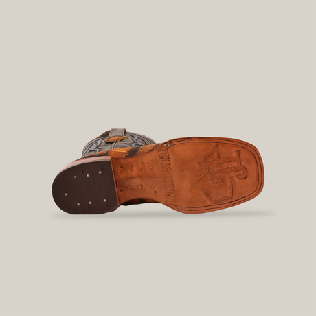 A lone Gator Print Rustic Honey - Square Toe boot rests on its side on a white background, highlighting the stamped logo near the heel of its tan sole and visible nail heads. This complements the rugged, dark brown texture of its premium cowhide leather upper.