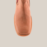 The Prime Suede Sand Square Toe is a tan leather cowboy boot with detailed stitching and a square toe, viewed from the top against a light background. This fashion-forward piece adds a rugged charm to any wardrobe.