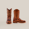 The Handtooled Leave Orix Square Toe cowboy boots, crafted from rich cowhide leather, feature detailed floral patterns. With one boot upright and the other tilted to display the design, these handcrafted boots showcase a thick heel and embody traditional Western craftsmanship.