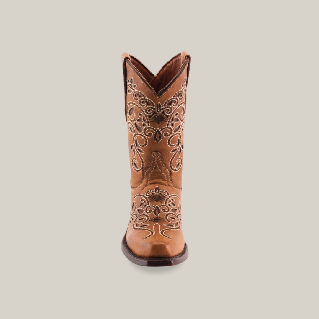 The Carola Tabaco - Snip Toe boot is a single brown cowboy boot made of premium leather, adorned with detailed white embroidery on the shaft and foot. It features a low heel and pull straps on either side, set against a simple white background.