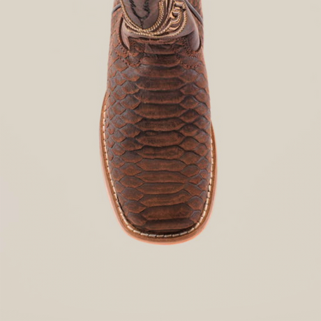 Close-up of a matte brown cowboy boot named Python Print, with textured python print on cowhide leather, detailed stitching, and a rounded square toe, set against a white background.