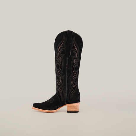 Against a white backdrop, the Amara Black Suede cowboy boot shines with intricate embroidery, a tall shaft, snip toe, and elegant wooden heel.