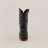 A front-facing view of a single Caiman Belly Print Black Square Toe cowboy boot exhibits an intricate black leather design, a pointed toe, and a light brown sole set against a plain white backdrop—ideal for cowboy enthusiasts.