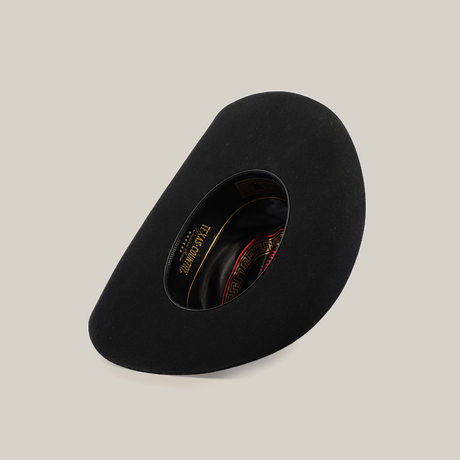 A 6X Dallas Black hat, crafted from sheep wool with a smooth surface and wide brim, lies showcasing its interior. The lining boasts a red and gold pattern alongside the brand label, highlighting Western sophistication.