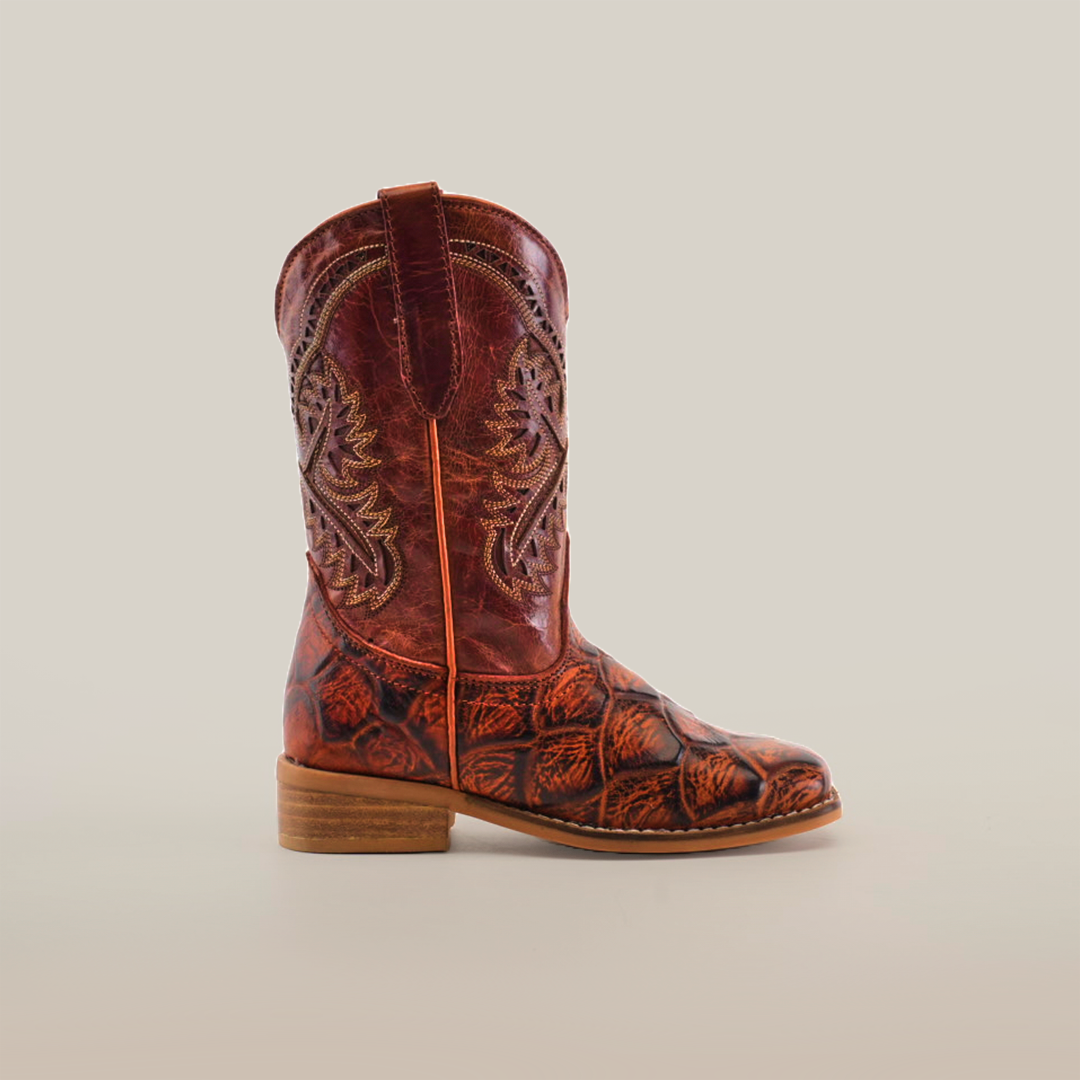 A single Pirarucu Bass Print Cogñac Square Toe cowboy boot made of premium brown leather features intricate shaft patterns and bass print texture on the lower part. Positioned on a plain light background with a low wooden heel and square toe, it faces left.