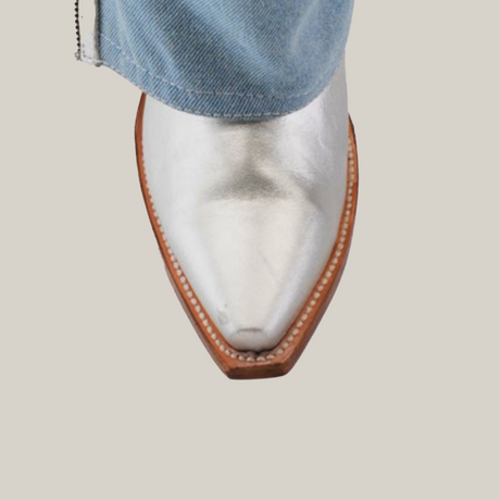 The image showcases the Bella Denim Silver – Tall Shaft with a snip toe and brown sole, elegantly peeking out from light blue Bella Denim against a sleek, light gray background.