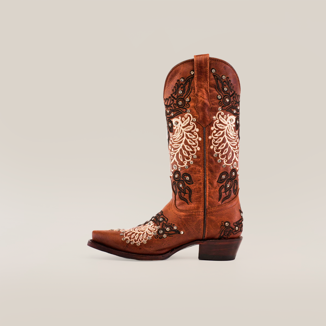 The Faenza Crystals Tabaco boot, with a snip toe and mid shaft, showcases intricate white and black floral embroidery on a plain brown boot. It exudes rustic elegance with subtle crystal embellishments.