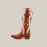 The Valentina Cogñac Tall Shaft boot, made from premium leather, features intricate white stitching and decorative patterns on the shaft. With a Western flair, it boasts a snip toe and low heel, all framed against a plain white background.