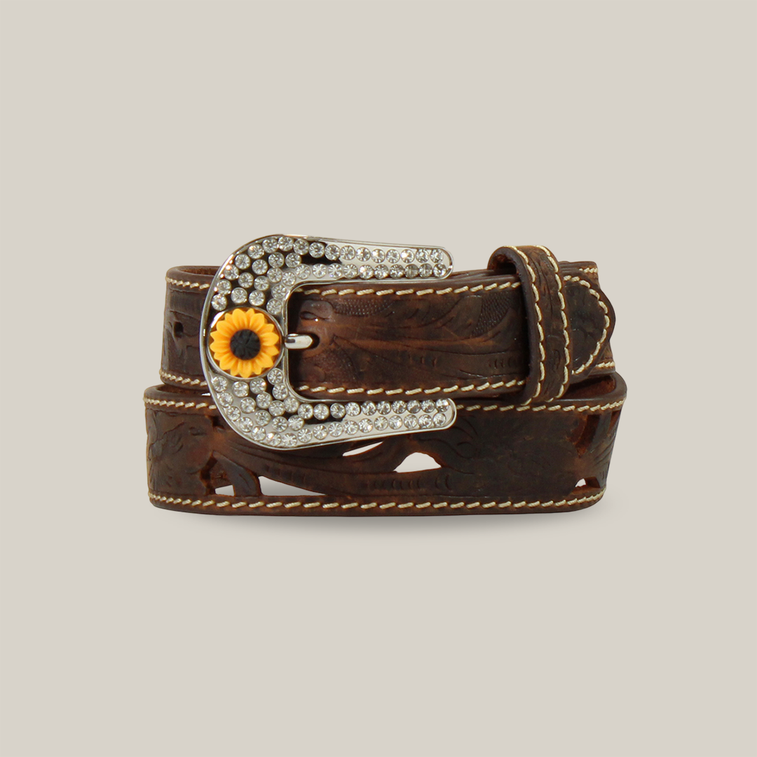 The Angel Ranch Western Girls Belt in brown (D130004002) features decorative stitching, a large silver buckle with sparkling gems, and a sunflower detail. Perfect for cowgirls, it epitomizes Western flair. The belt is rolled up against a light backdrop.