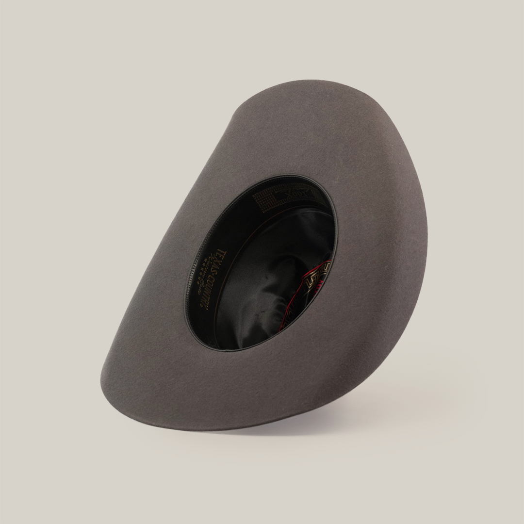 A 6X Leandro Oxford gray felt hat, made of premium sheeps wool, is displayed from the underside showing its black inner lining. Resembling a cowboy hat, its tilted on a white background with a label inside featuring gold lettering and a small flag.