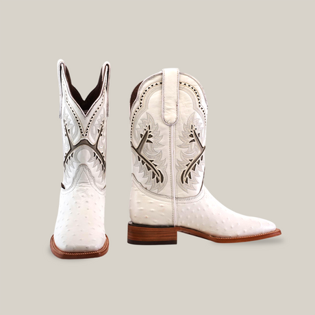 The Karoo Ostrich Print White - Square Toe boots are crafted from premium leather with intricate patterns and stitching. The right boot stands upright, and the left is angled diagonally. Featuring a wooden heel and a pointed toe, they exude timeless elegance.